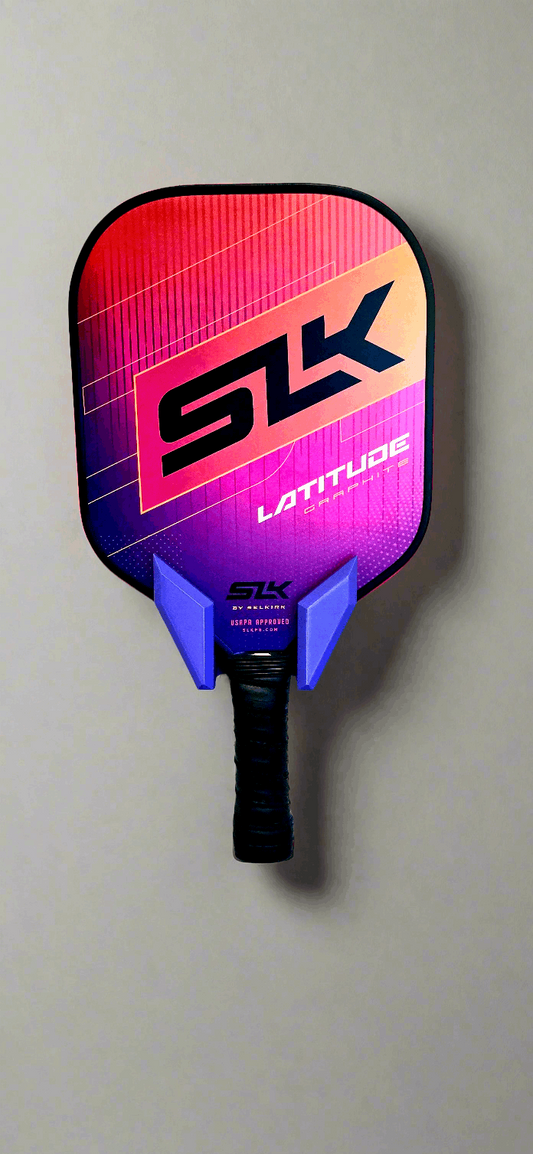 Vibrant pickleball paddle on wall display - Tarbon Designs' sleek, colorful SLK Latitude model showcases dynamic design.